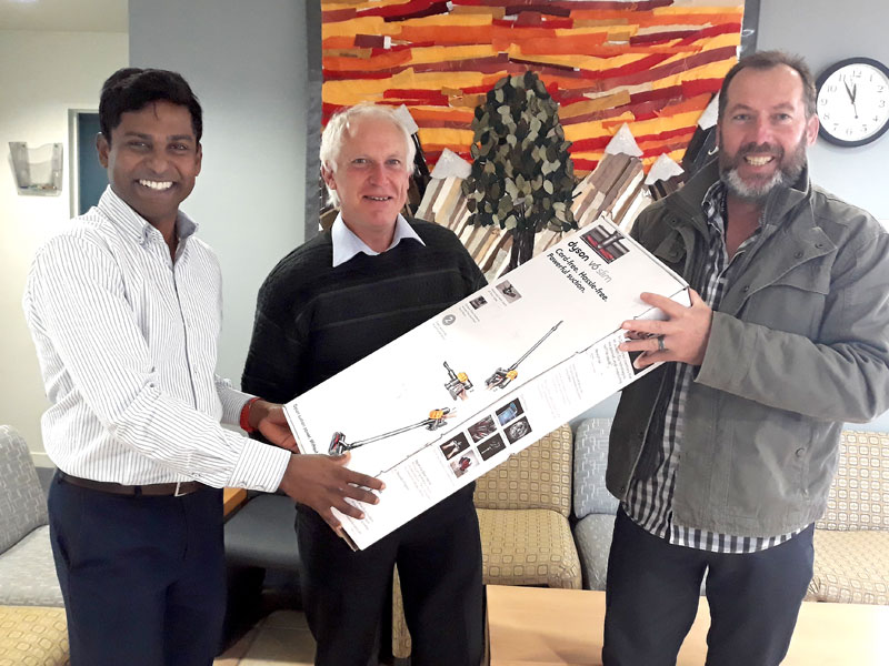 Chris Els receives the vacuum cleaner from Yasa Panagoda. Looking on (centre) is Redwood Primary School Principal John Stackhouse. 